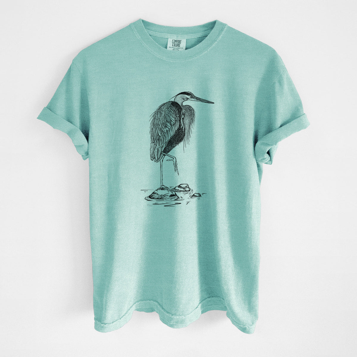 Chalky mint Comfort Colors t-shirt laid flat, printed with a detailed black ink illustration of a great blue heron standing on rocks.