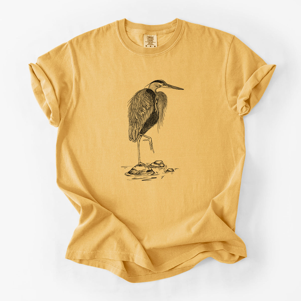Golden wheat yellow Comfort Colors t-shirt laid flat, printed with a detailed black ink illustration of a great blue heron standing on rocks.