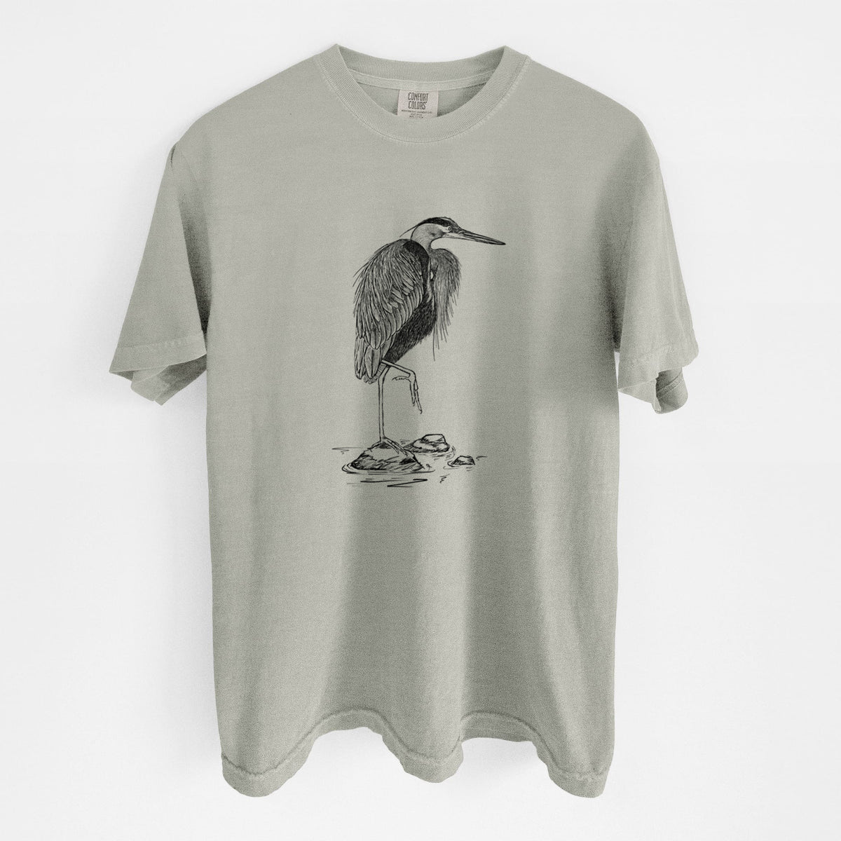 Sandstone beige Comfort Colors t-shirt laid flat, printed with a detailed black ink illustration of a great blue heron standing on rocks.