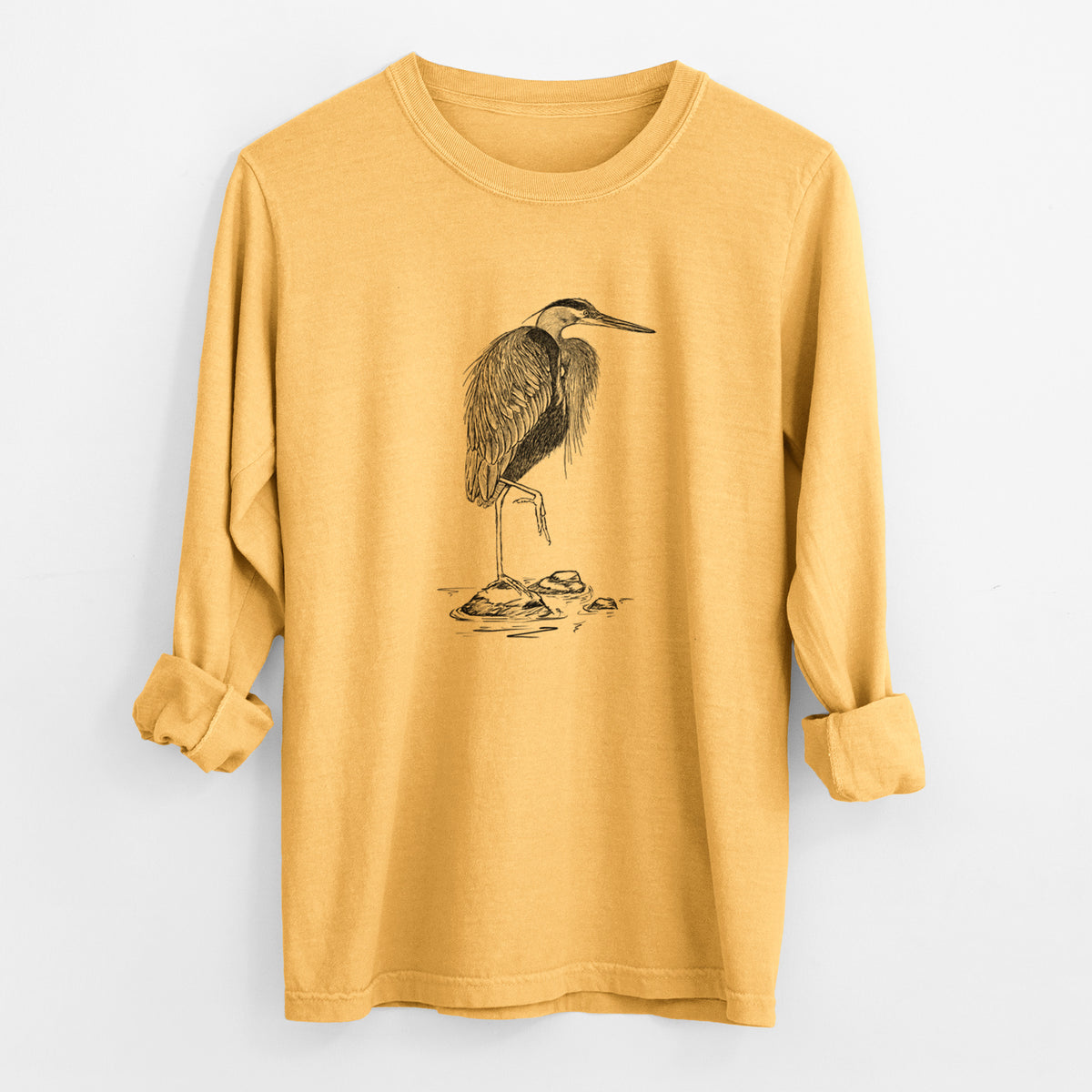 Golden wheat yellow Comfort Colors long sleeve shirt laid flat with the cuffs rolled, printed with a detailed black ink illustration of a great blue heron standing on rocks.