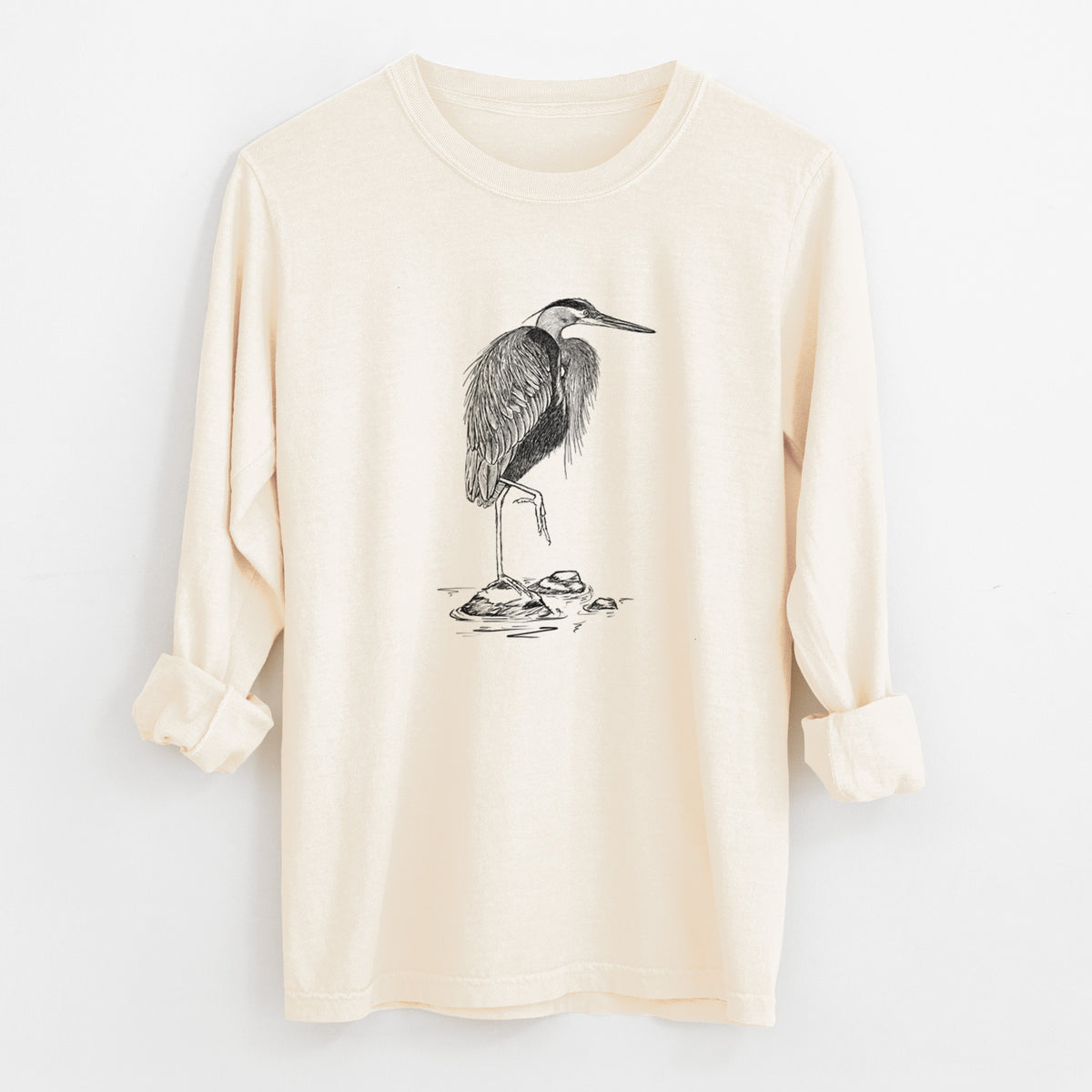 Ivory Comfort Colors long sleeve shirt laid flat with the cuffs rolled, printed with a detailed black ink illustration of a great blue heron standing on rocks.