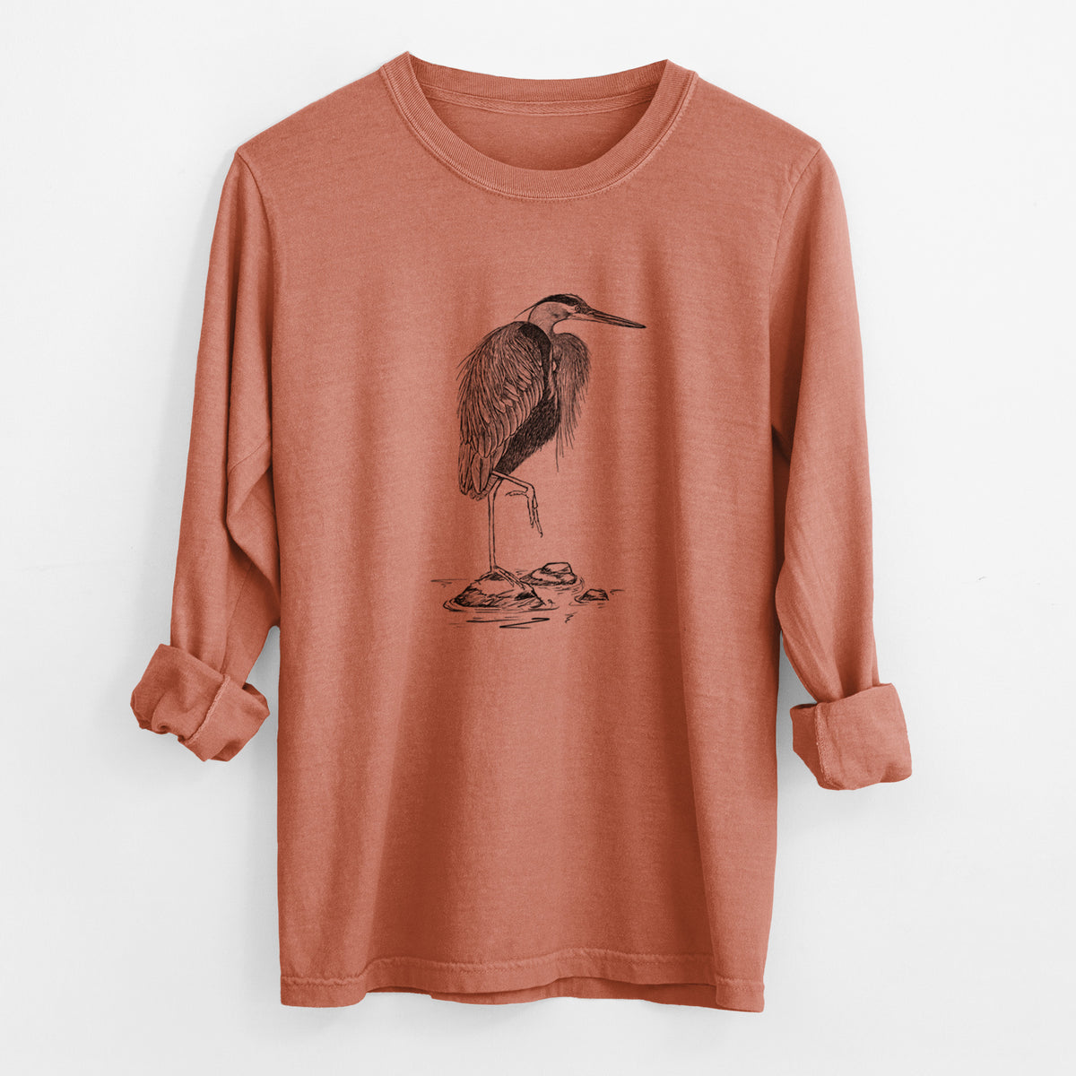 Yam burnt orange Comfort Colors long sleeve shirt laid flat with the cuffs rolled, printed with a detailed black ink illustration of a great blue heron standing on rocks.
