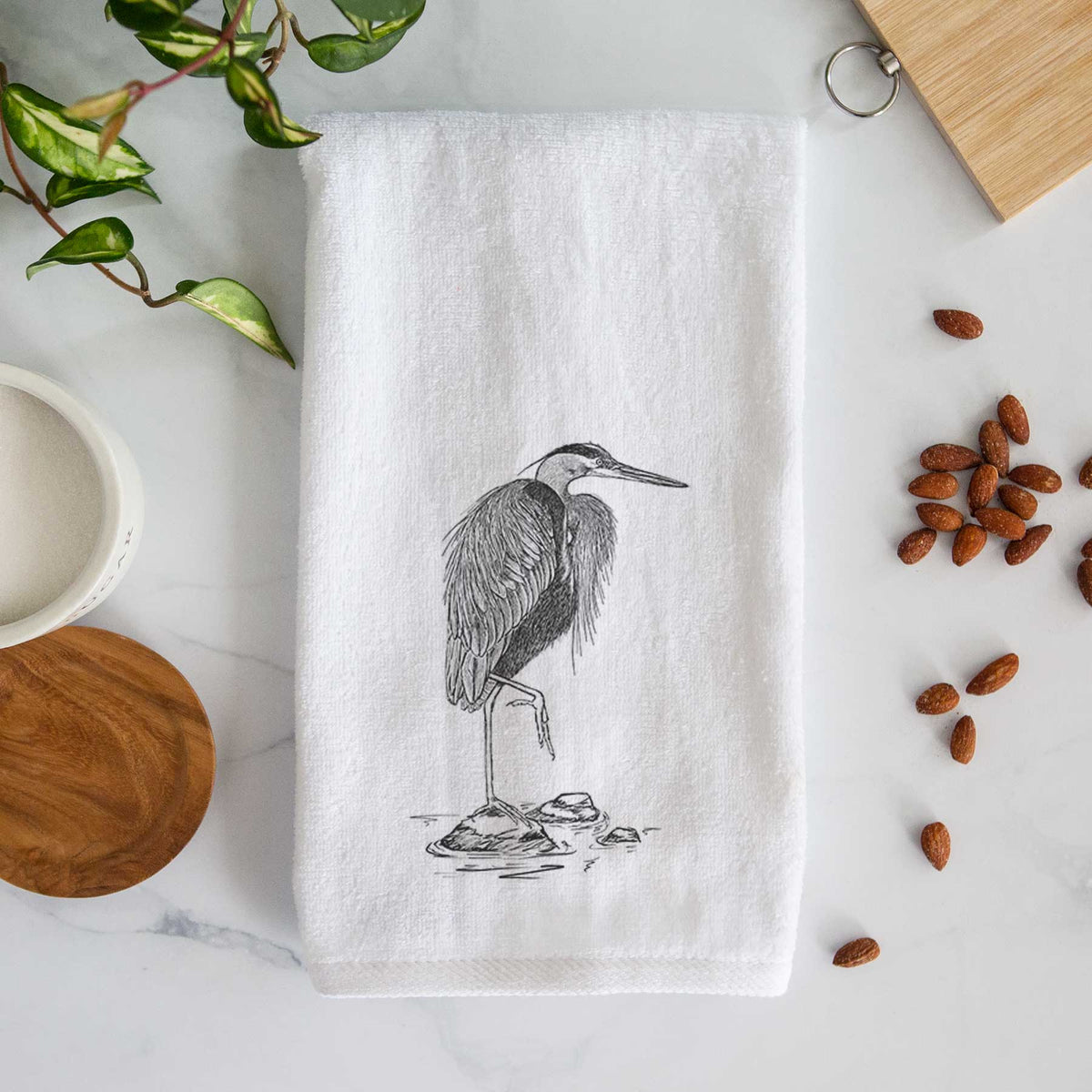 White hand towel printed with a detailed black ink illustration of a great blue heron standing on rocks.