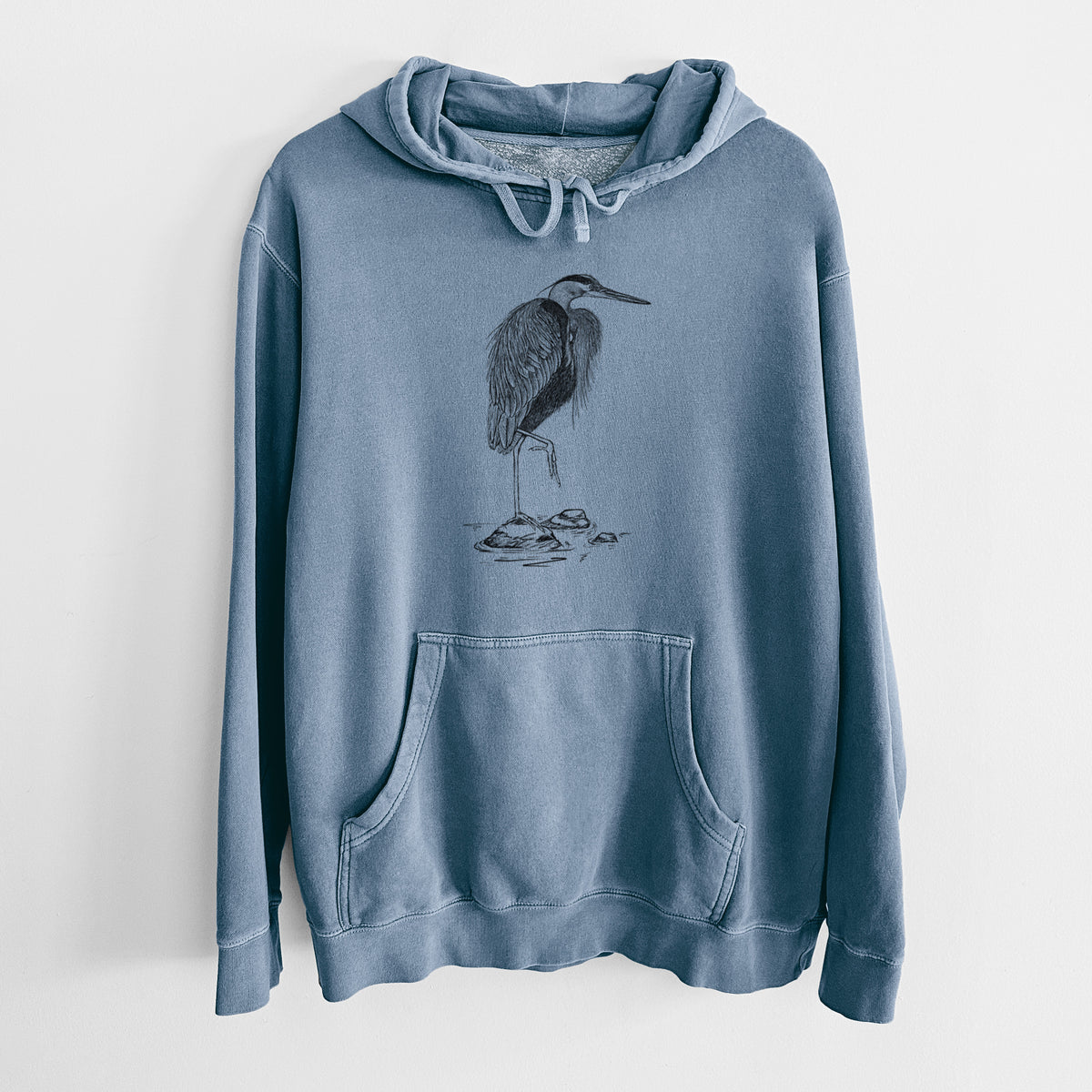 Slate blue pigment dyed hoodie laid flat, printed with a detailed black ink illustration of a great blue heron standing on rocks.