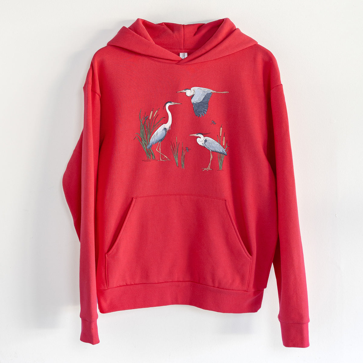 Great Blue Herons in the Cattails - Statement Midweight Hoodie in Cherry Red, hanging on a white wall, with a front kangaroo pocket and no drawcords.