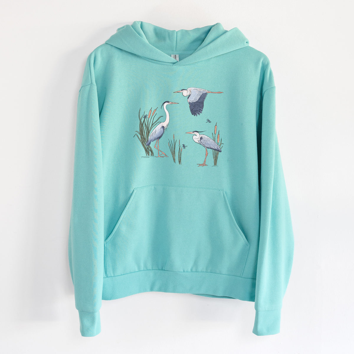 Great Blue Herons in the Cattails - Statement Midweight Hoodie in Seafoam, hanging on a white wall, with a front kangaroo pocket and no drawcords.