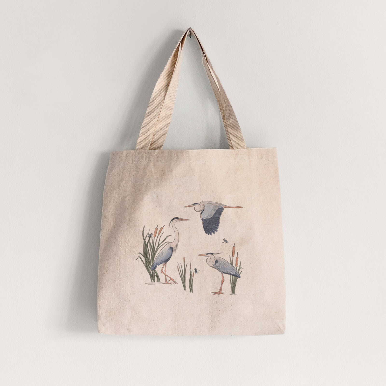 Natural canvas tote bag printed with a full-color illustration of three great blue herons among cattails, one in flight.