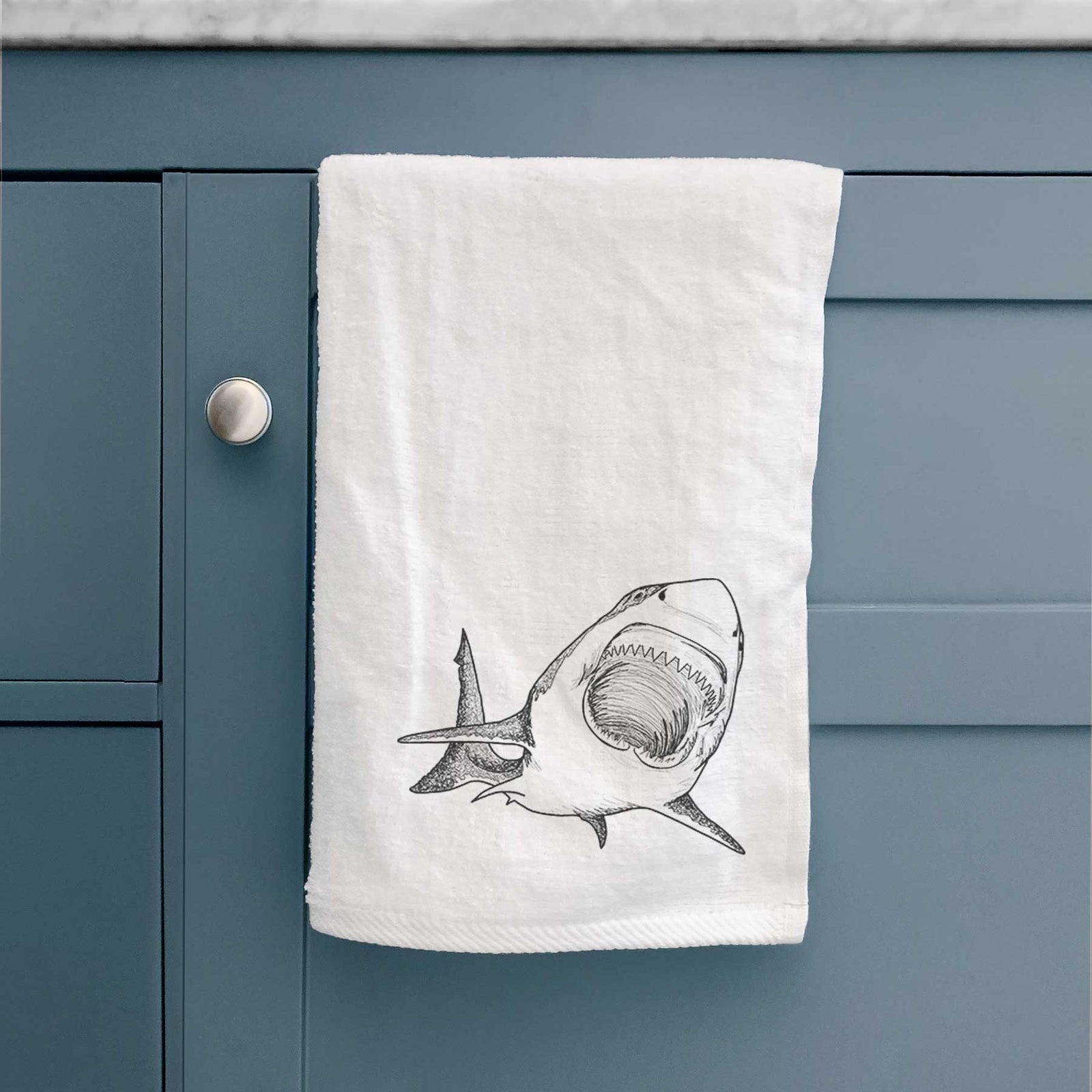 White hand towel printed with a black ink illustration of a great white shark swimming toward the viewer with its mouth open.