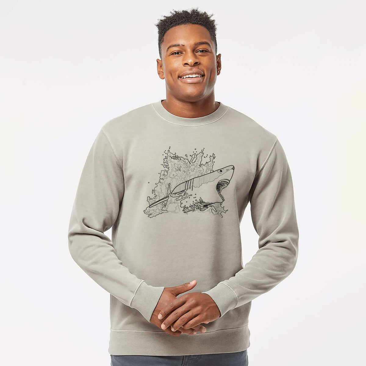 Model wearing a cement grey pigment dyed crewneck sweatshirt printed with a black ink illustration of a great white shark breaking through a splash of water.