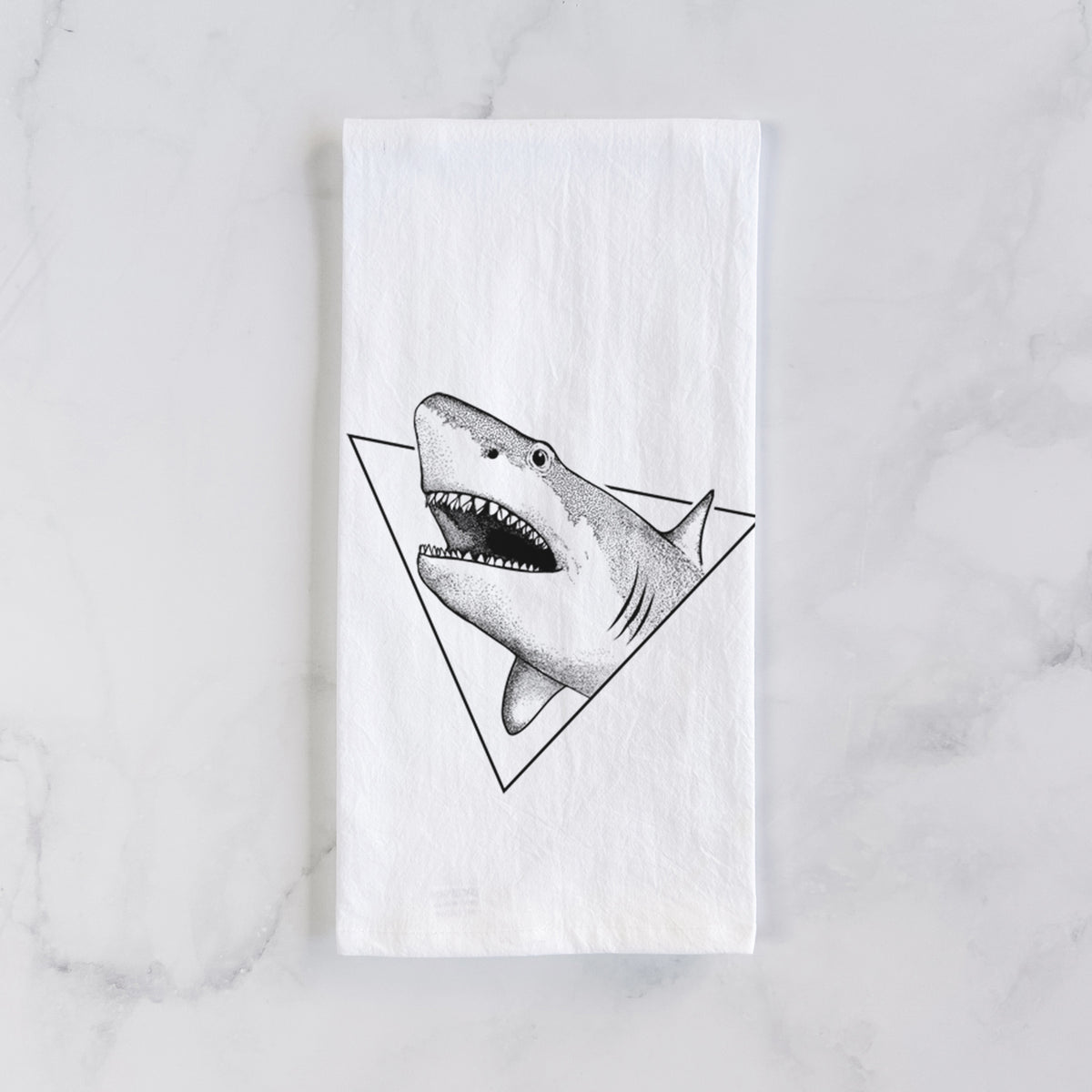 White cotton tea towel laid flat on marble, printed with a black ink great white shark bursting out of a triangle outline with its mouth open.