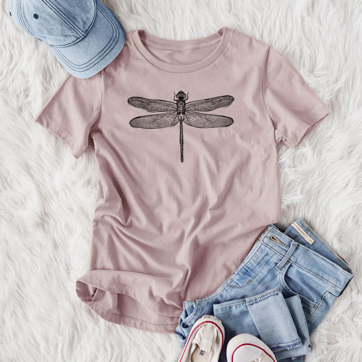 Women's relaxed fit cotton t-shirt printed with a detailed black ink illustration of a green darner dragonfly with its wings spread, seen from above, styled flat on a white faux fur rug with jeans.