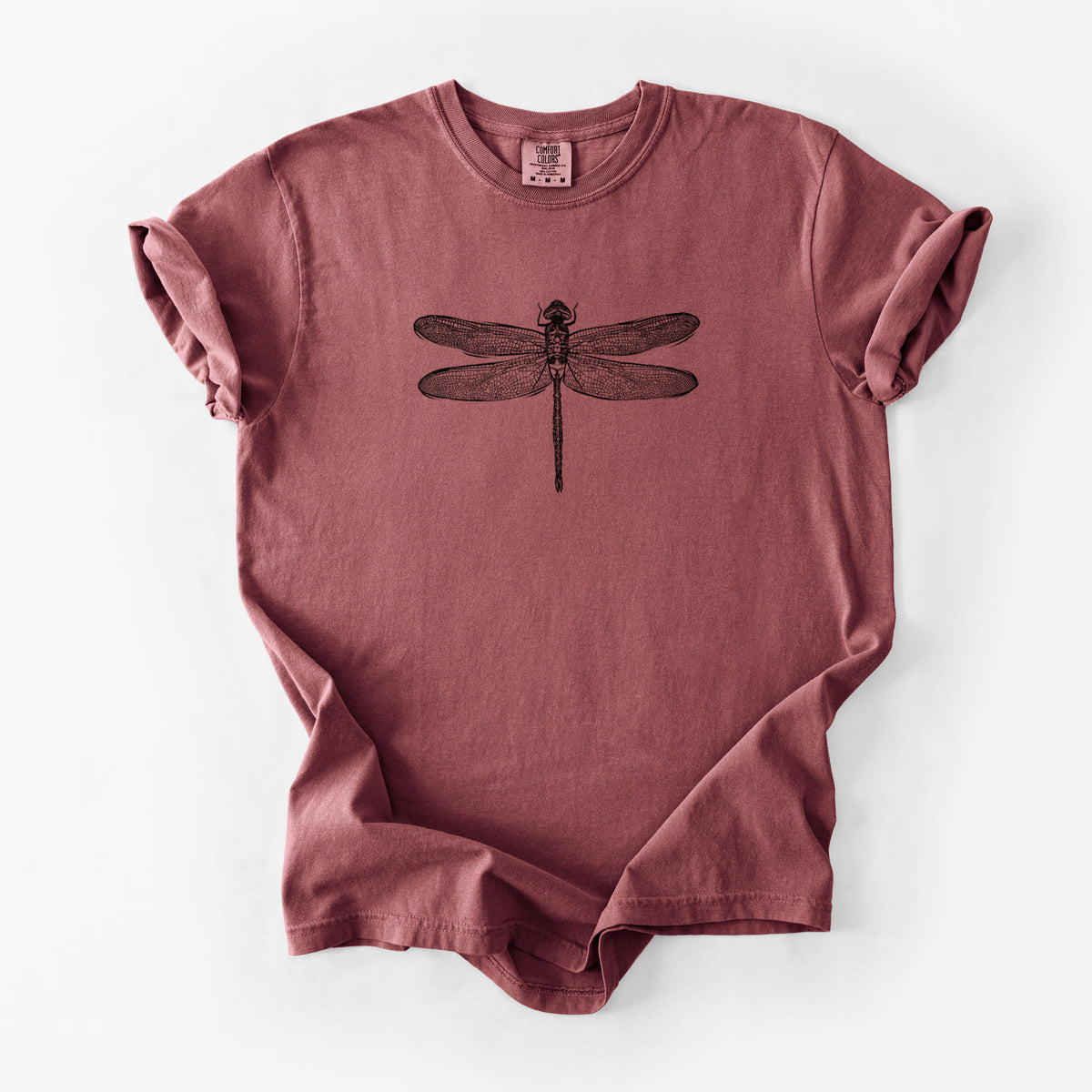 Brick red Comfort Colors t-shirt laid flat, printed with a detailed black ink illustration of a green darner dragonfly with its wings spread, seen from above.