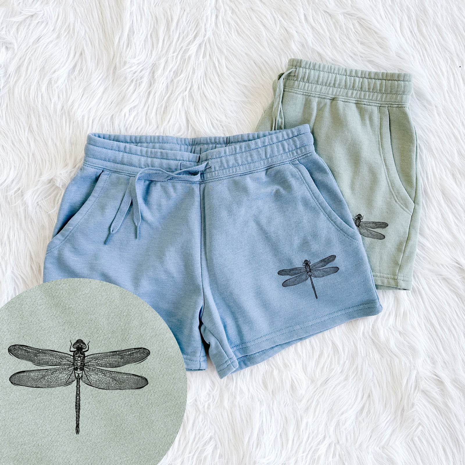 Two pairs of Cali Wave shorts in different colors printed with a detailed black ink illustration of a green darner dragonfly with its wings spread, seen from above, with a close-up of the print.