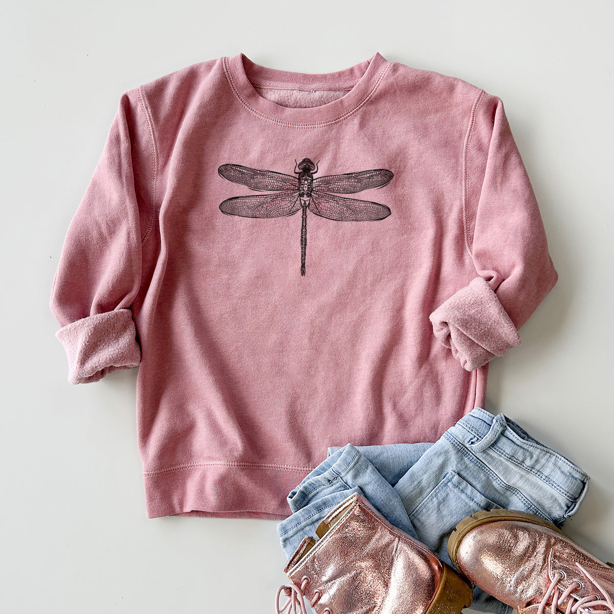 Youth crewneck sweatshirt printed with a detailed black ink illustration of a green darner dragonfly with its wings spread, seen from above, styled flat with jeans and boots.