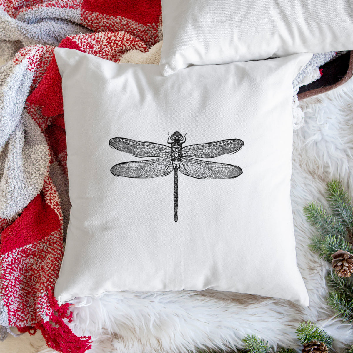 White pillow cover printed with a detailed black ink illustration of a green darner dragonfly with its wings spread, seen from above, on a woven chair.