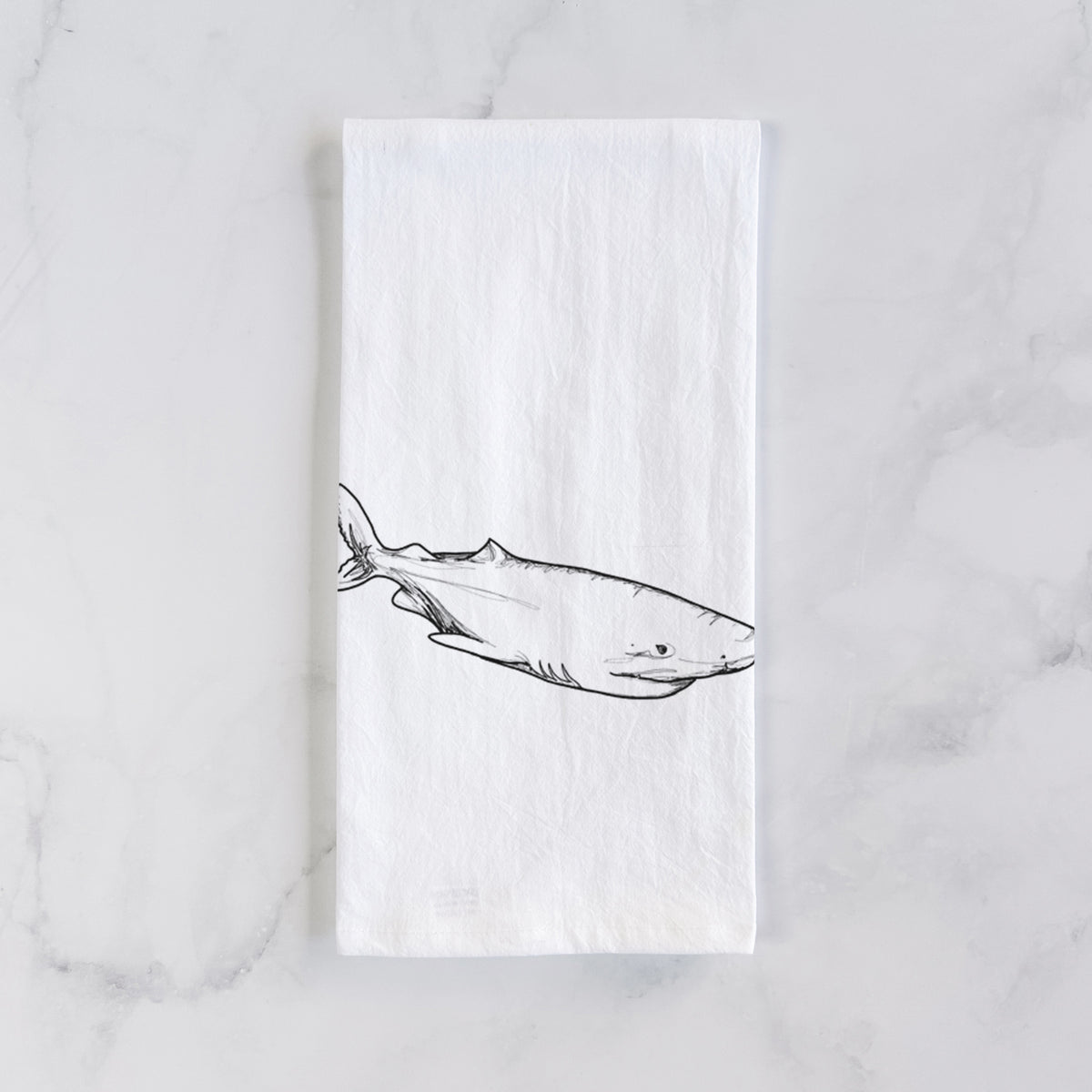 White cotton tea towel laid flat on marble, printed with a black ink illustration of a Greenland shark swimming.