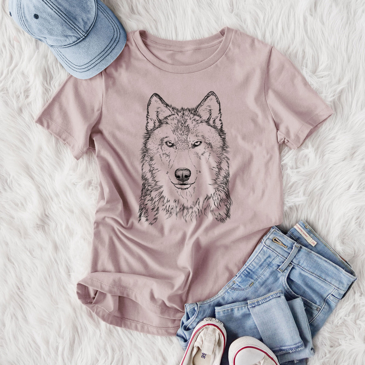 Women's relaxed fit cotton t-shirt printed with a detailed black ink portrait of a grey wolf facing forward, styled flat on a white faux fur rug with jeans.