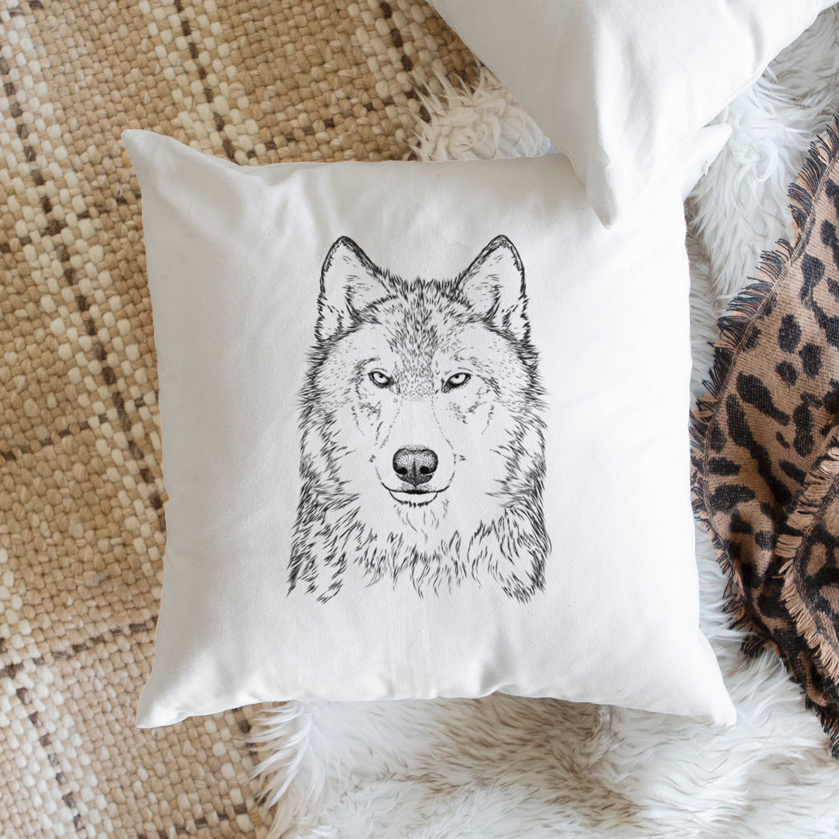 White pillow cover printed with a detailed black ink portrait of a grey wolf facing forward, on a woven chair.