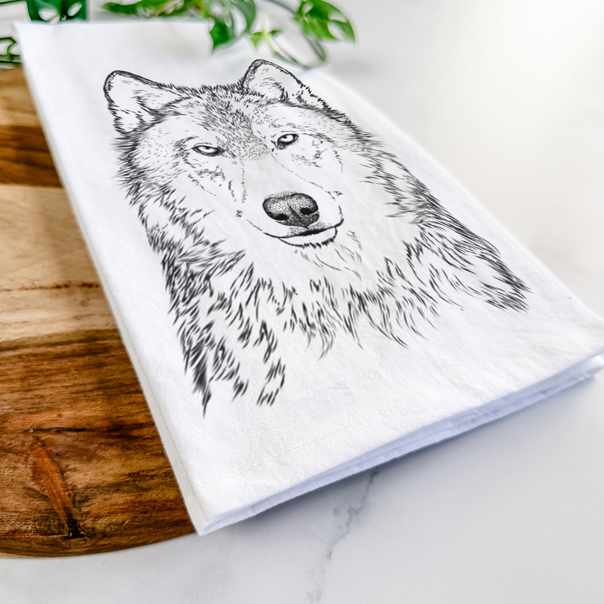 Close-up of a folded white tea towel on a wooden board, showing a detailed black ink portrait of a grey wolf facing forward.