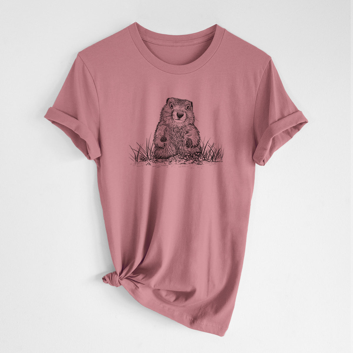 Mauve pink lightweight cotton t-shirt laid flat with the sleeves rolled, printed with a black ink illustration of a groundhog peeking out of its burrow among grass.