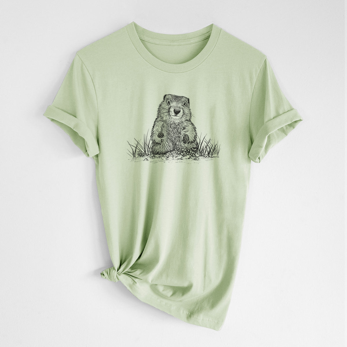 Spring green lightweight cotton t-shirt laid flat with the sleeves rolled, printed with a black ink illustration of a groundhog peeking out of its burrow among grass.