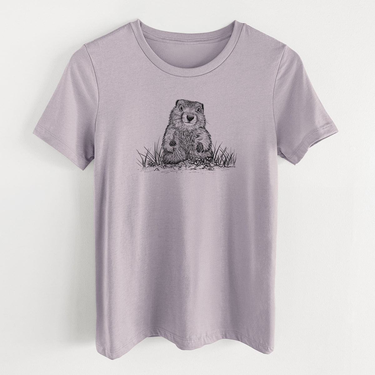 Light violet women's relaxed fit cotton t-shirt laid flat, printed with a black ink illustration of a groundhog peeking out of its burrow among grass.