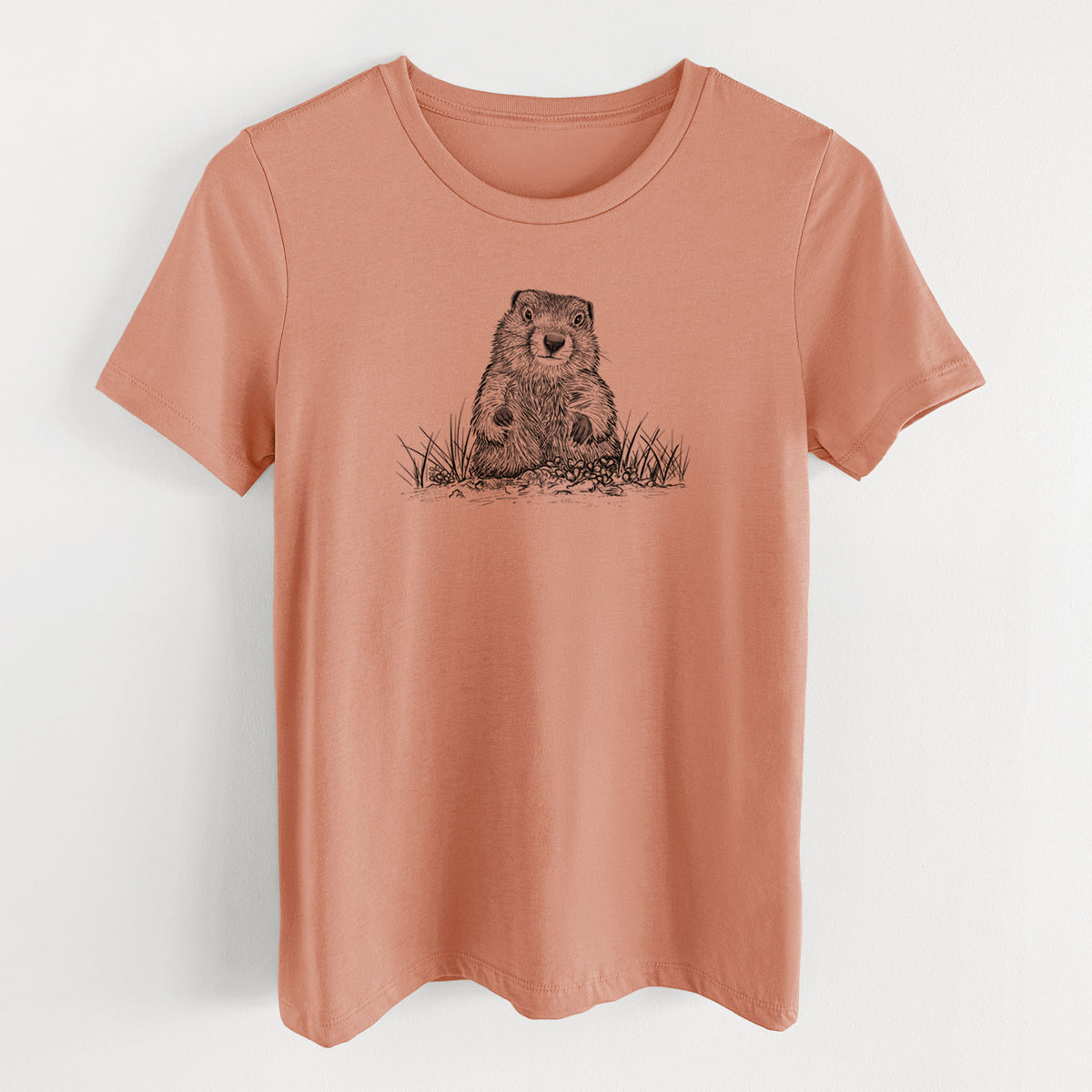 Terracotta orange women's relaxed fit cotton t-shirt laid flat, printed with a black ink illustration of a groundhog peeking out of its burrow among grass.