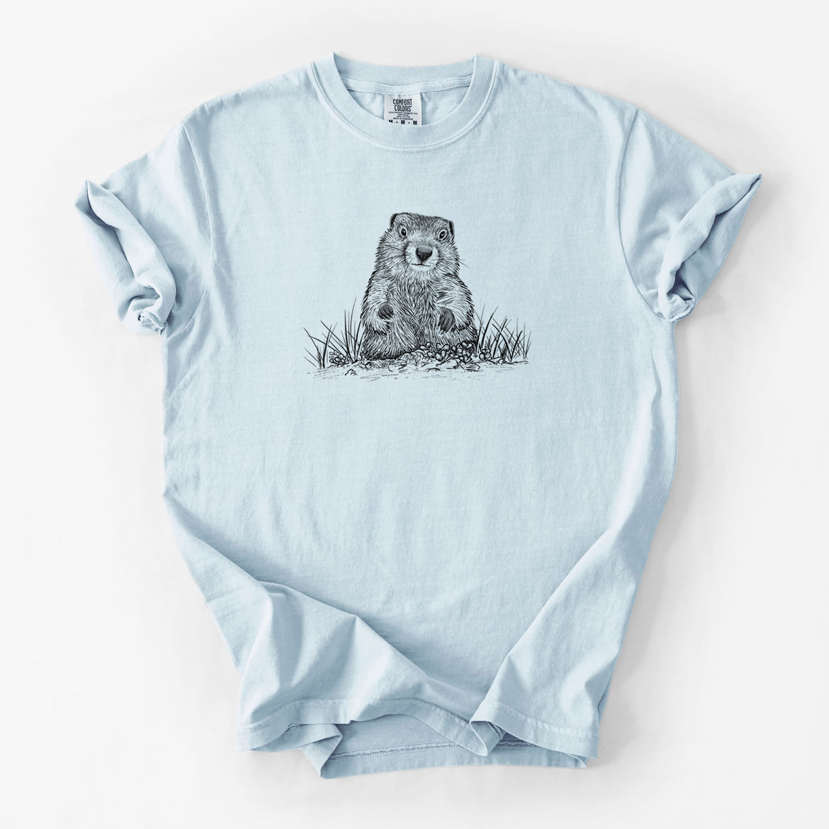 Chambray blue Comfort Colors t-shirt laid flat, printed with a black ink illustration of a groundhog peeking out of its burrow among grass.