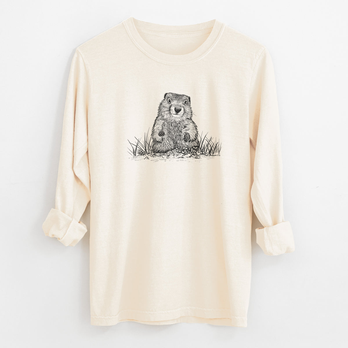 Ivory Comfort Colors long sleeve shirt laid flat with the cuffs rolled, printed with a black ink illustration of a groundhog peeking out of its burrow among grass.