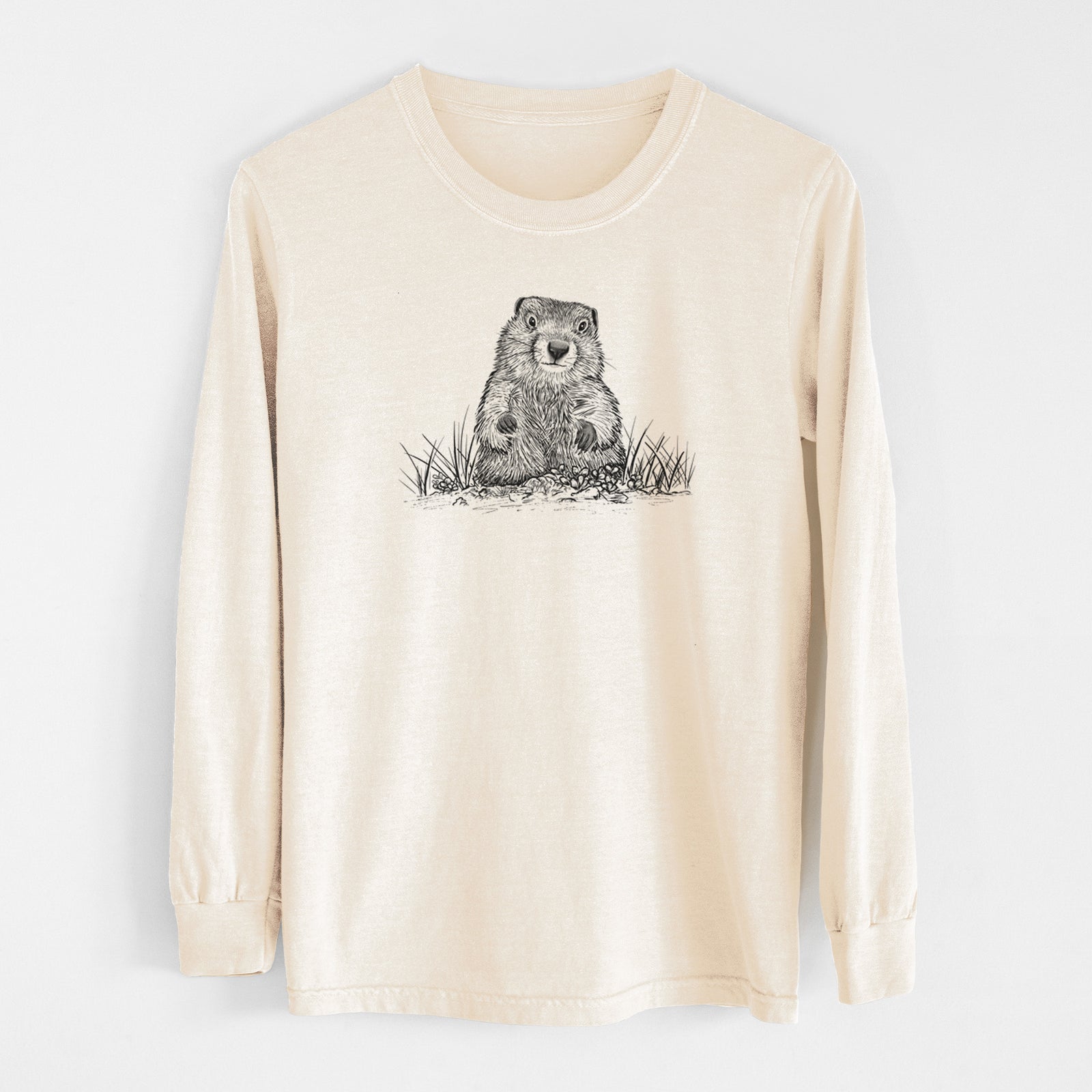 Ivory Comfort Colors long sleeve shirt laid flat, printed with a black ink illustration of a groundhog peeking out of its burrow among grass.
