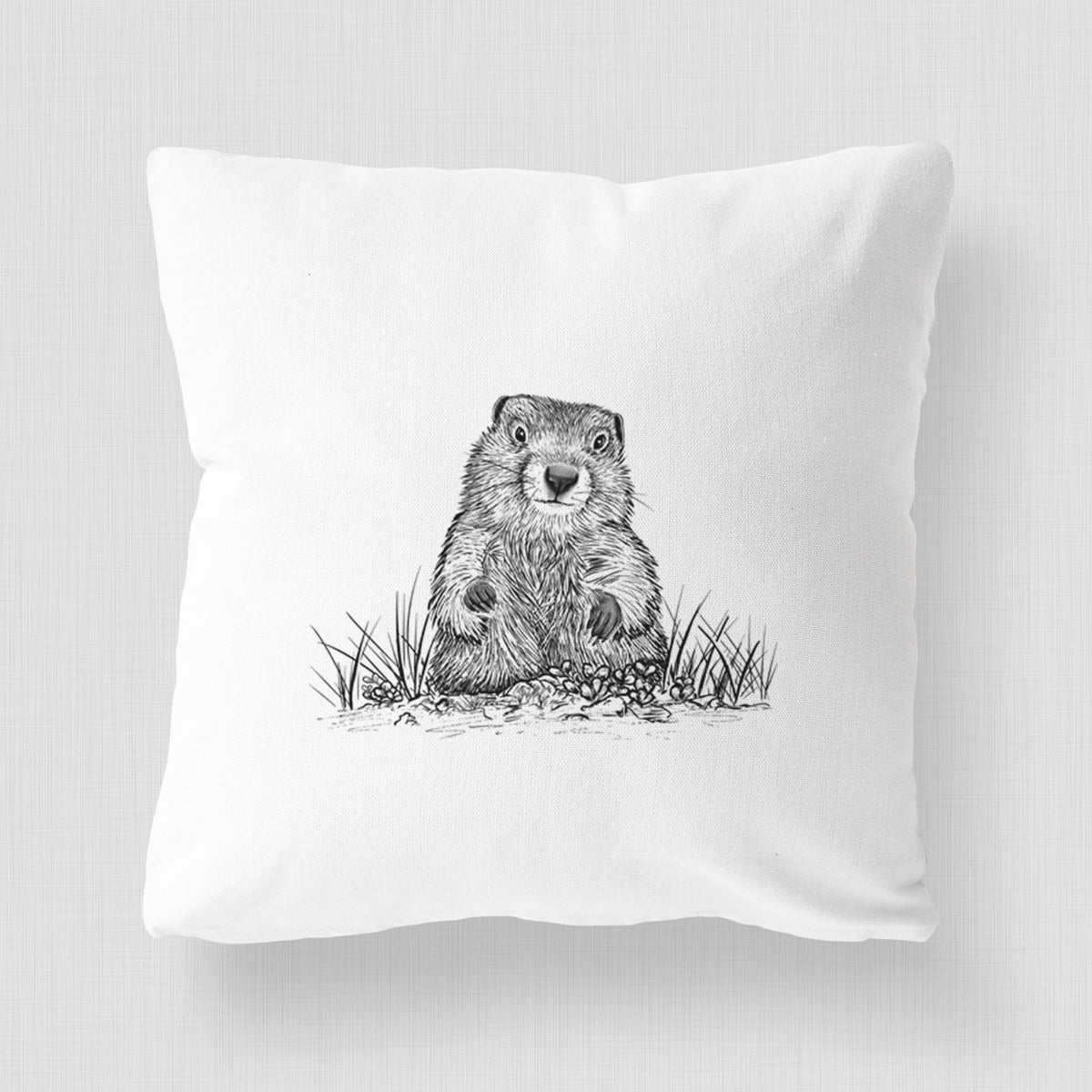 White pillow cover printed with a black ink illustration of a groundhog peeking out of its burrow among grass.