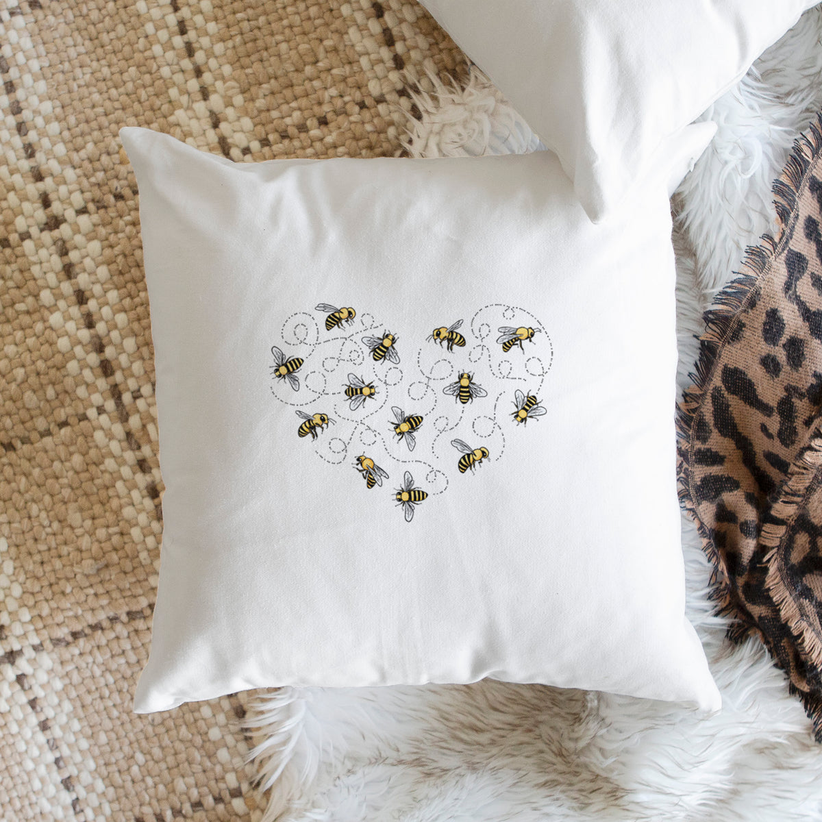 White pillow cover printed with a heart shape made of small bees and looping flight trails, on a woven chair.
