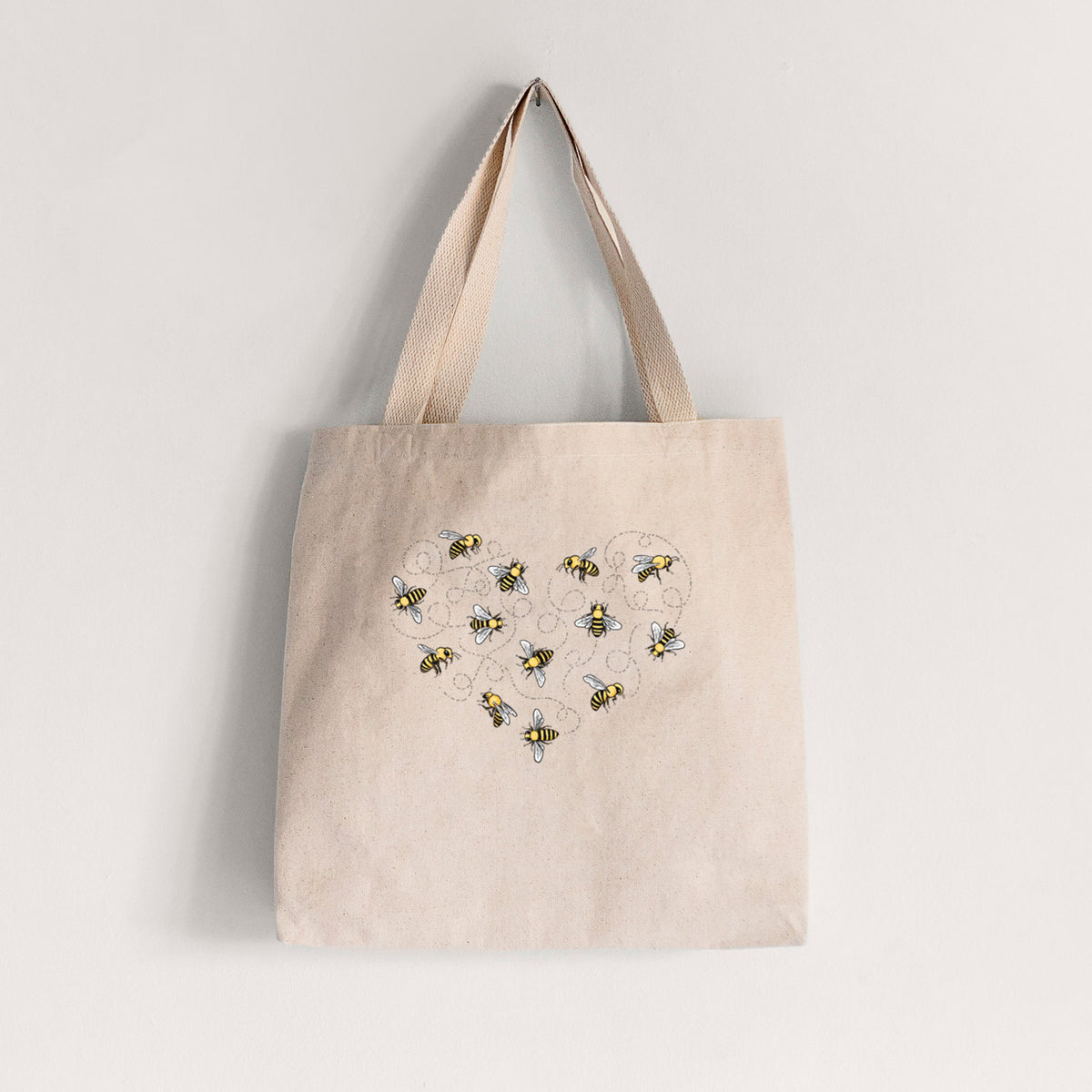 Natural canvas tote bag printed with a heart shape made of small bees and looping flight trails.