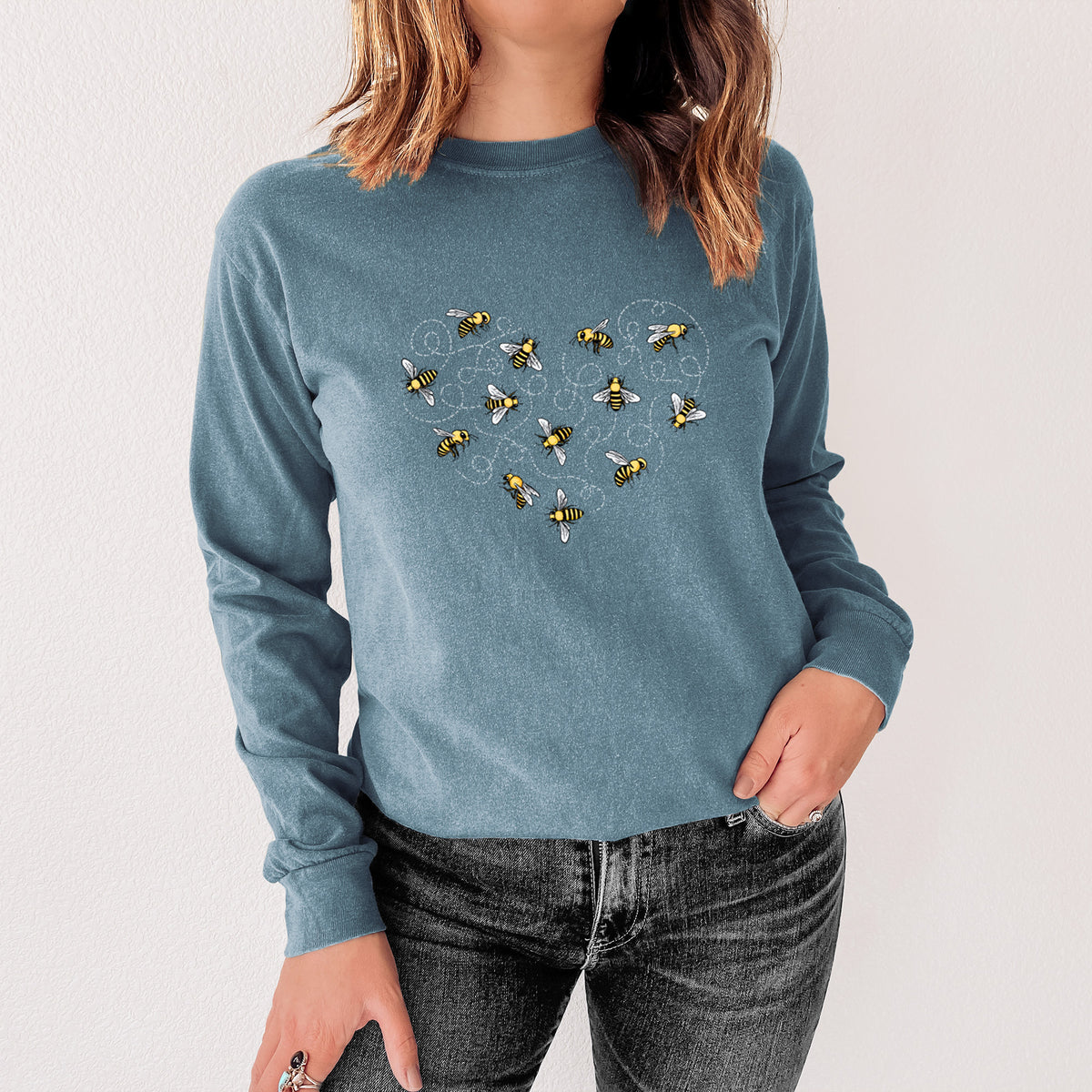 Steel blue Comfort Colors long sleeve shirt printed with a heart shape made of small bees and looping flight trails, shown in a lifestyle photo.