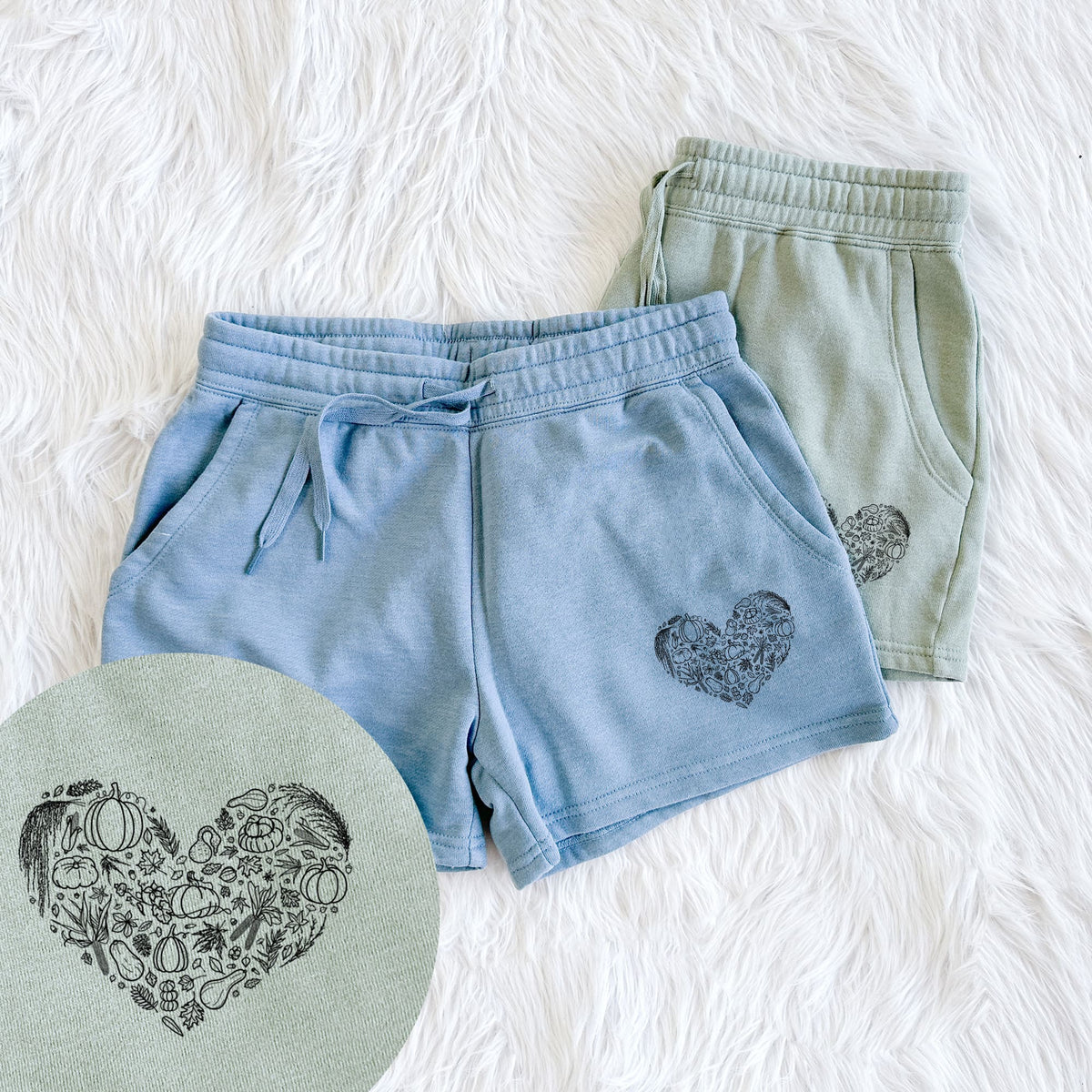 Two pairs of Cali Wave shorts in different colors printed with a heart shape filled with black ink autumn leaves, acorns, pumpkins and mushrooms, with a close-up of the print.
