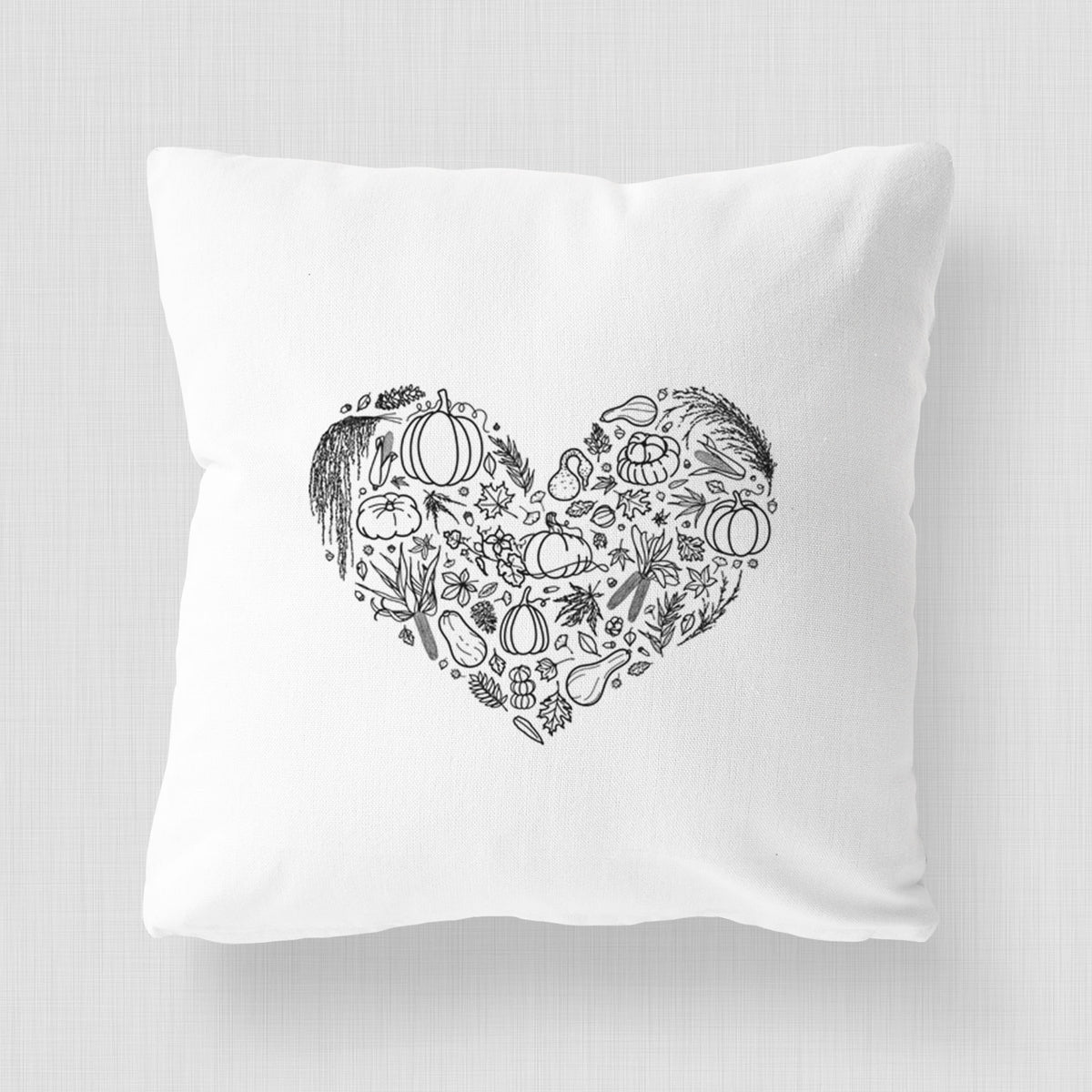 White pillow cover printed with a heart shape filled with black ink autumn leaves, acorns, pumpkins and mushrooms.
