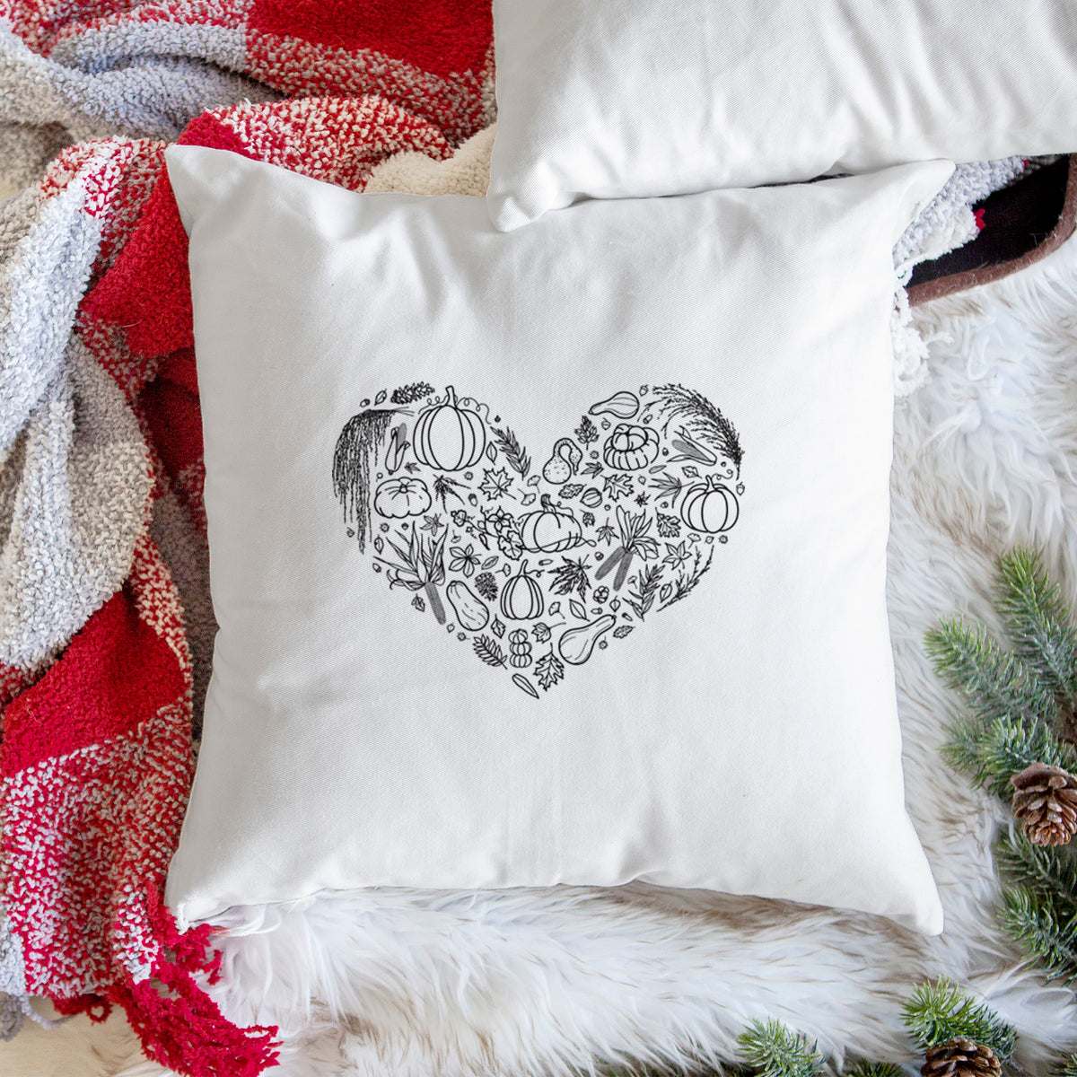 White pillow cover printed with a heart shape filled with black ink autumn leaves, acorns, pumpkins and mushrooms, on a woven chair.