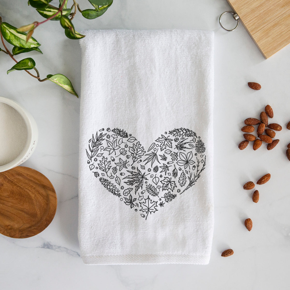 White hand towel printed with a heart shape filled with black ink autumn leaves.