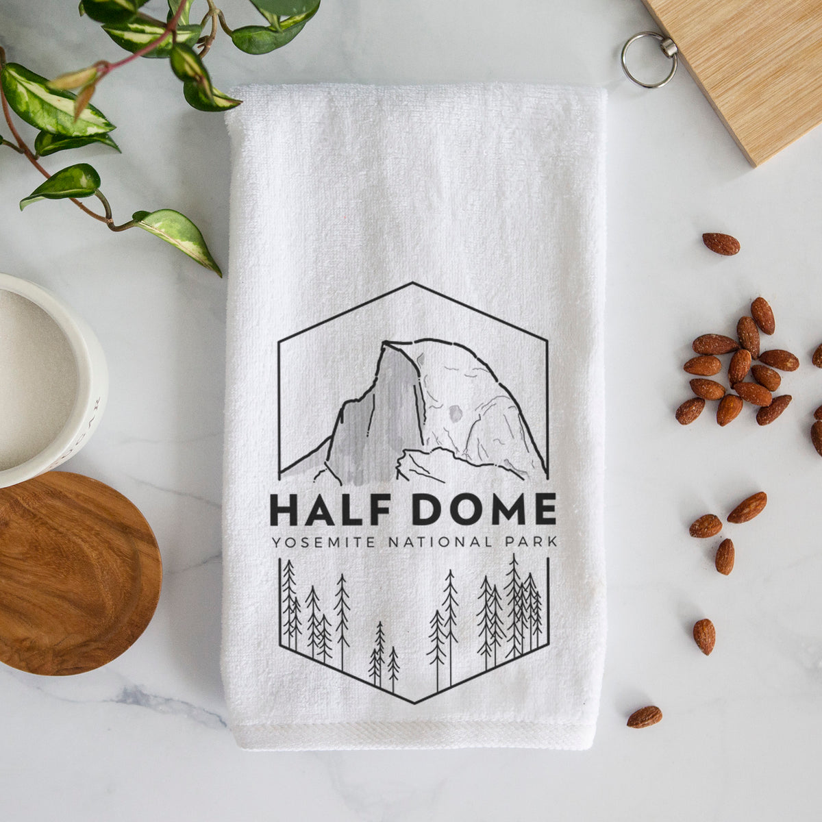 White hand towel printed with a black line art badge of Half Dome above a pine forest, with the words Half Dome, Yosemite National Park.