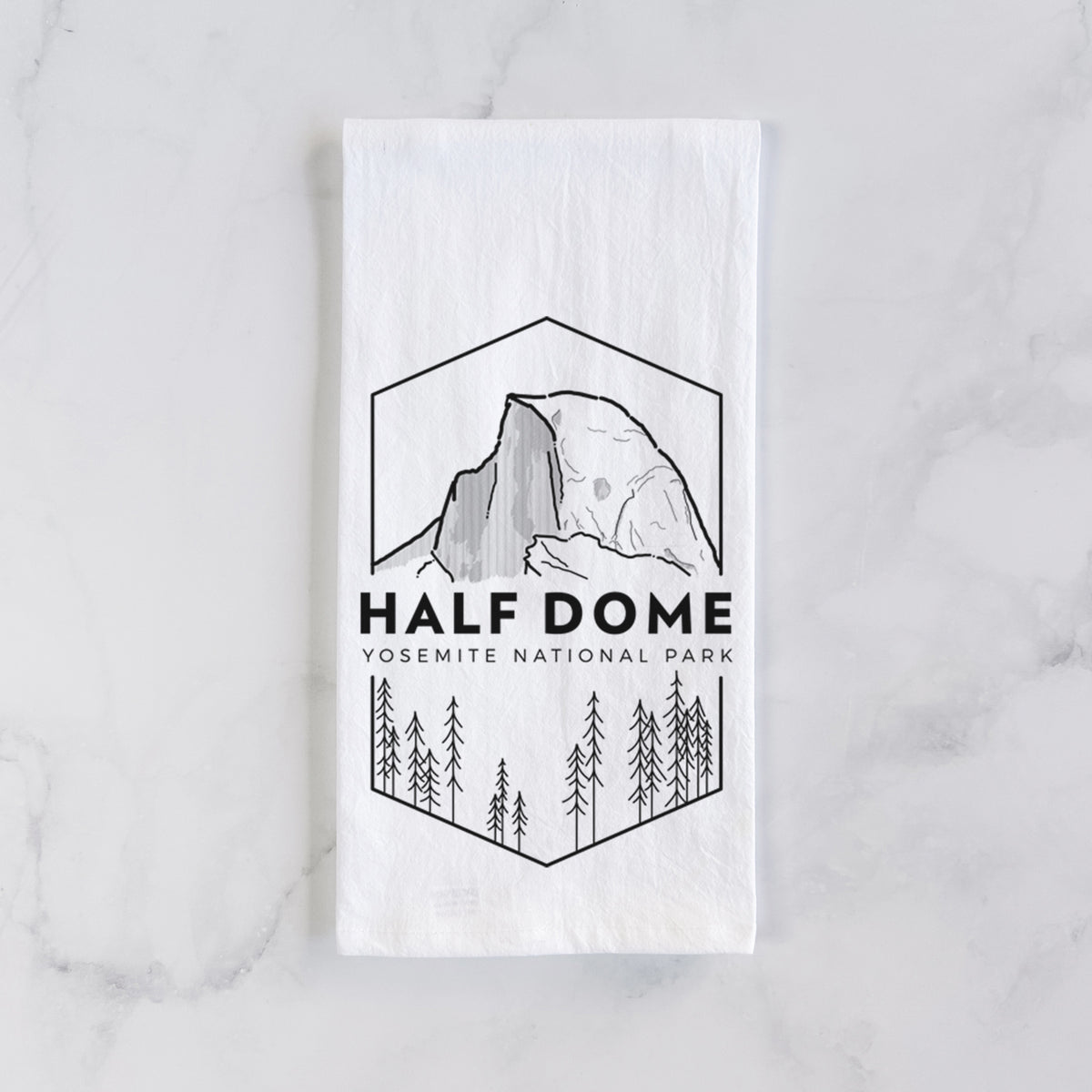 White cotton tea towel laid flat on marble, printed with a black line art badge of Half Dome above a pine forest, with the words Half Dome, Yosemite National Park.