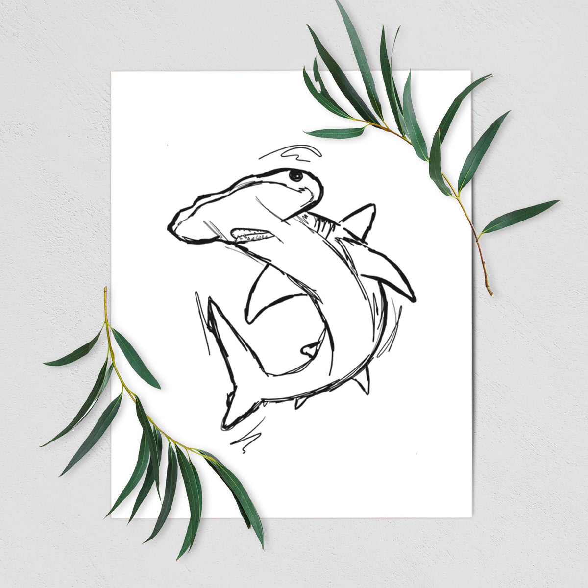 Art print of a black ink illustration of a hammerhead shark swimming in a curve, shown with eucalyptus leaves.