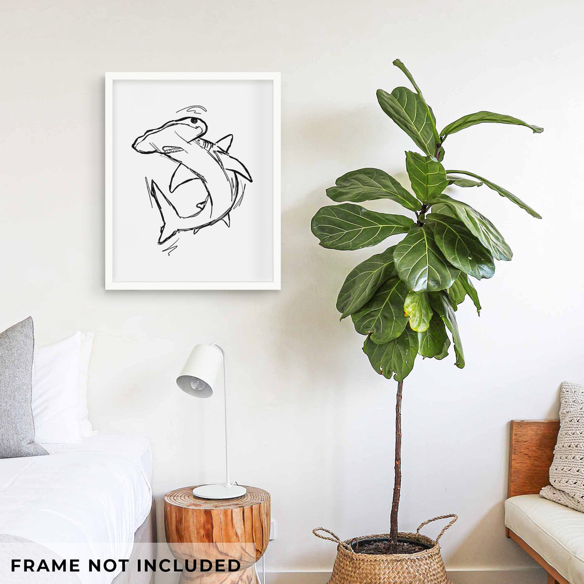 Art print of a black ink illustration of a hammerhead shark swimming in a curve, shown framed on a living room wall beside a potted plant. Frame not included.