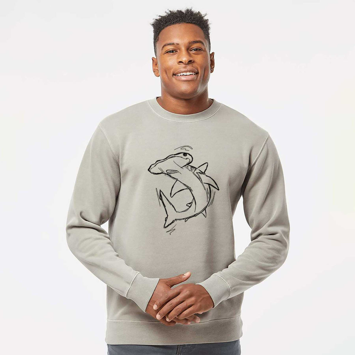 Model wearing a cement grey pigment dyed crewneck sweatshirt printed with a black ink illustration of a hammerhead shark swimming in a curve.