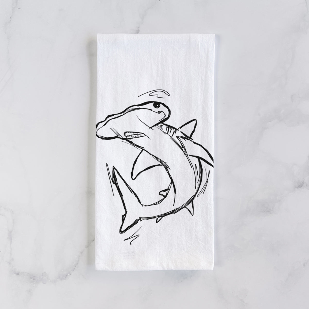 White cotton tea towel laid flat on marble, printed with a black ink illustration of a hammerhead shark swimming in a curve.