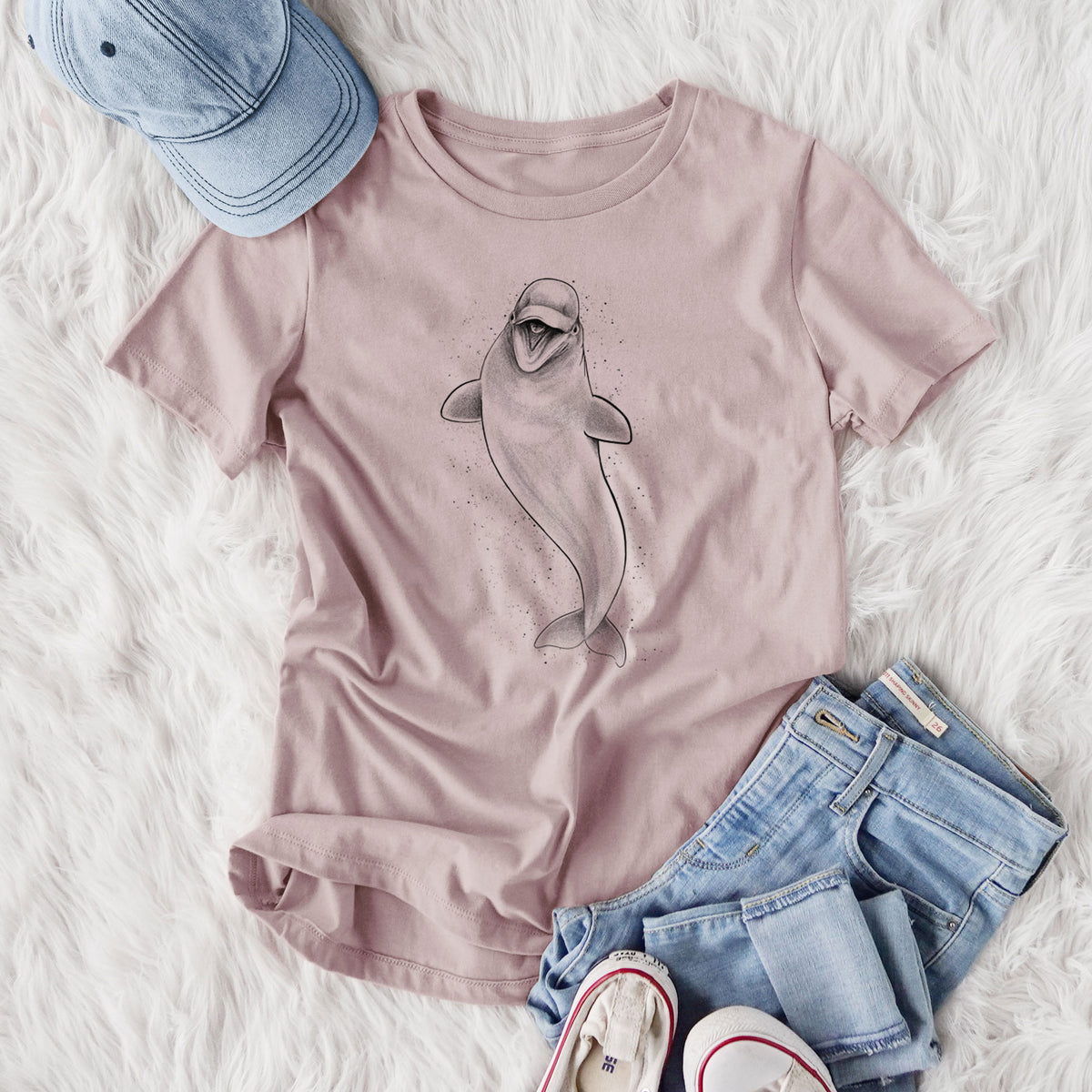 Women's relaxed fit cotton t-shirt printed with a black ink illustration of a smiling beluga whale swimming upward, styled flat on a white faux fur rug with jeans.
