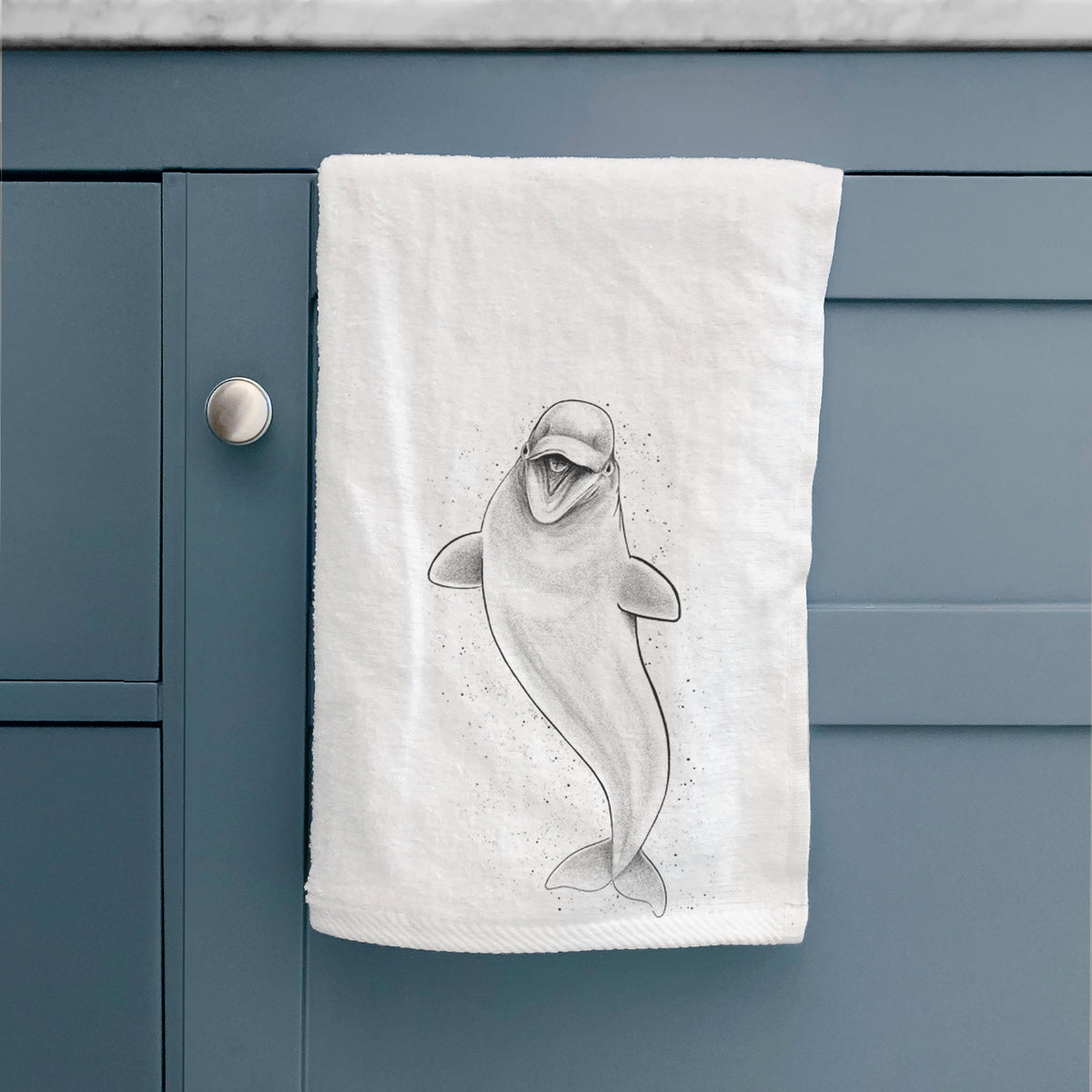 White hand towel printed with a black ink illustration of a smiling beluga whale swimming upward, hanging on a cabinet door.