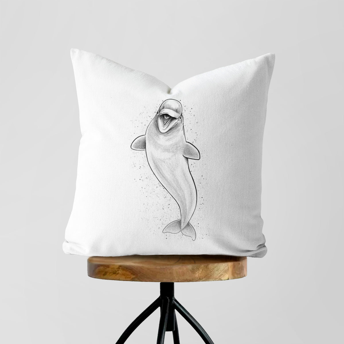 White pillow cover printed with a black ink illustration of a smiling beluga whale swimming upward, on a wooden stool.