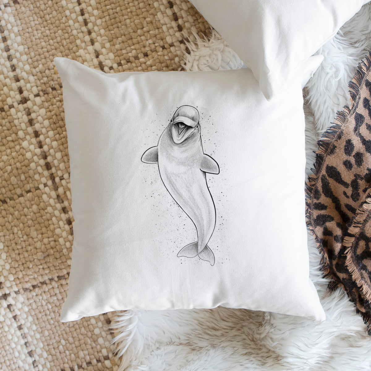 White pillow cover printed with a black ink illustration of a smiling beluga whale swimming upward, on a woven chair.
