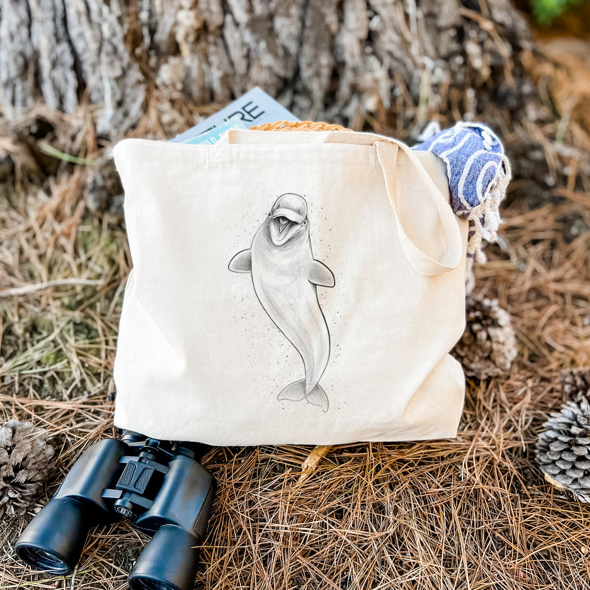 Canvas tote bag printed with a black ink illustration of a smiling beluga whale swimming upward, resting on dry grass beside a pair of binoculars.