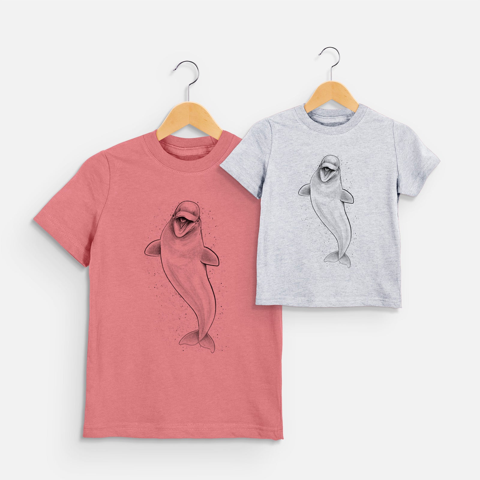 Two youth t-shirts in different colors on hangers, printed with a black ink illustration of a smiling beluga whale swimming upward.